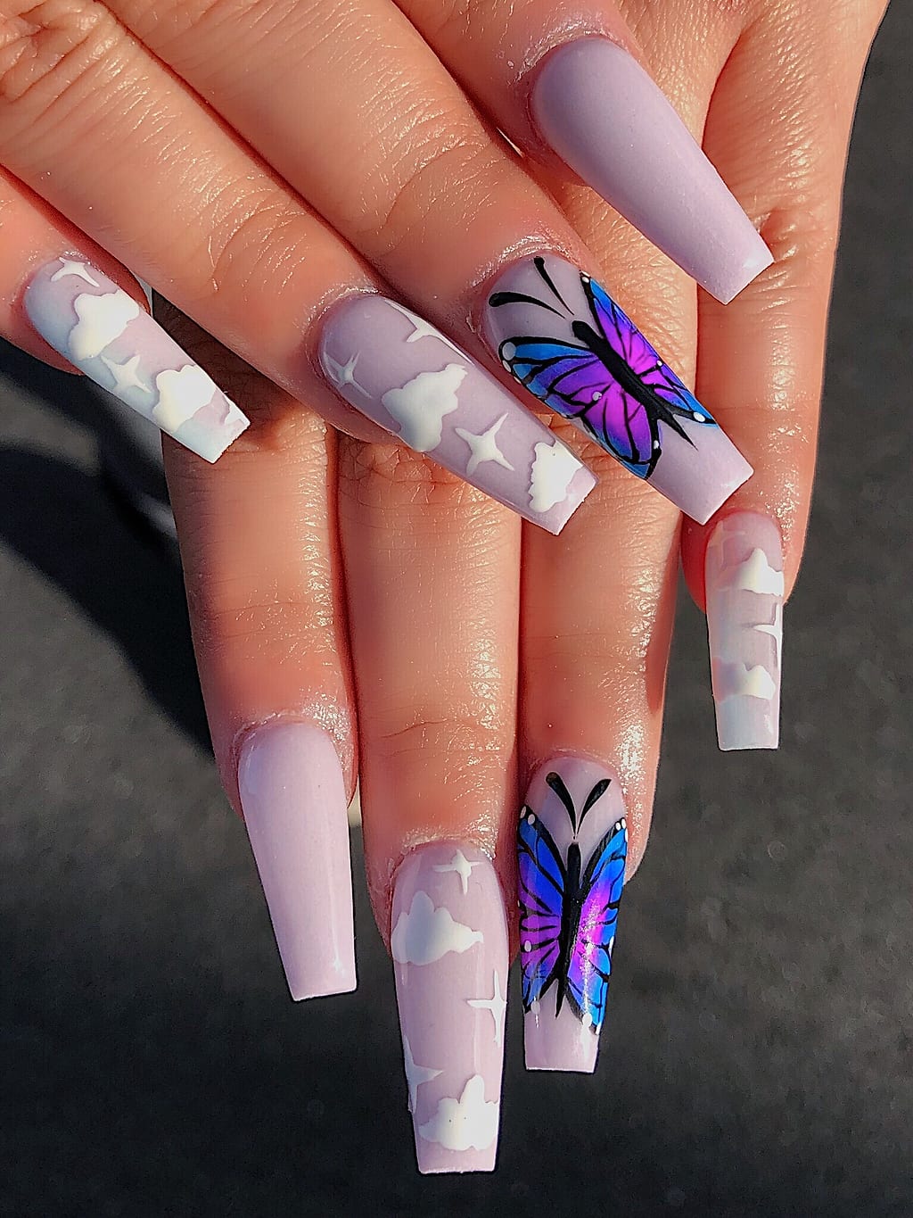 Nude coffin nails with a soft cloud pattern and purple butterfly accent at Palace Nail Spa