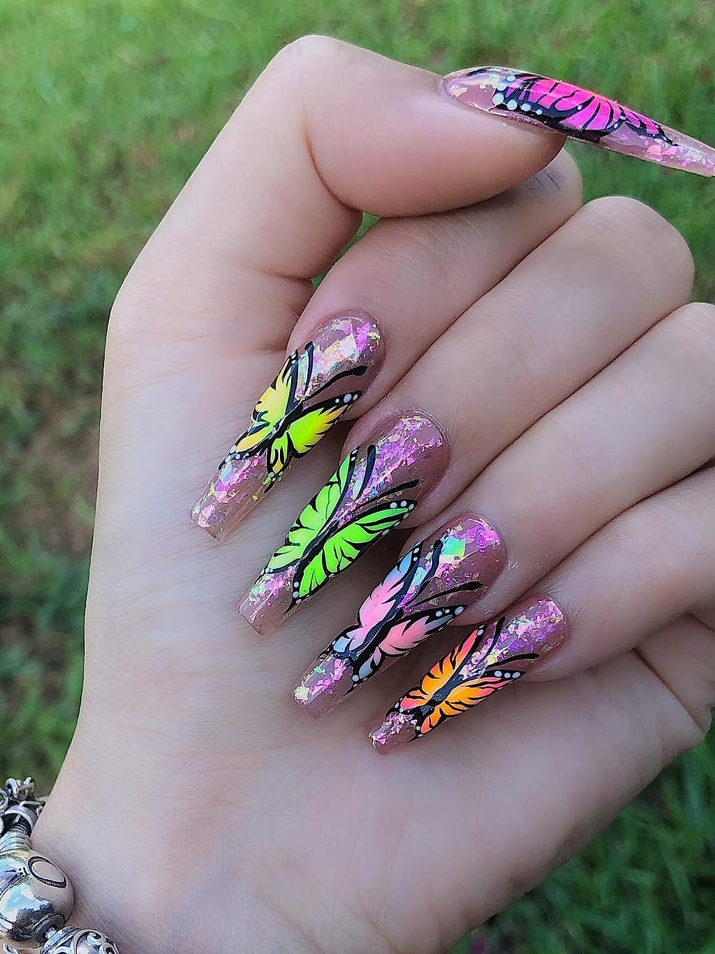 Pink glitter almond nails with colorful butterfly and floral art at Palace Nail Spa