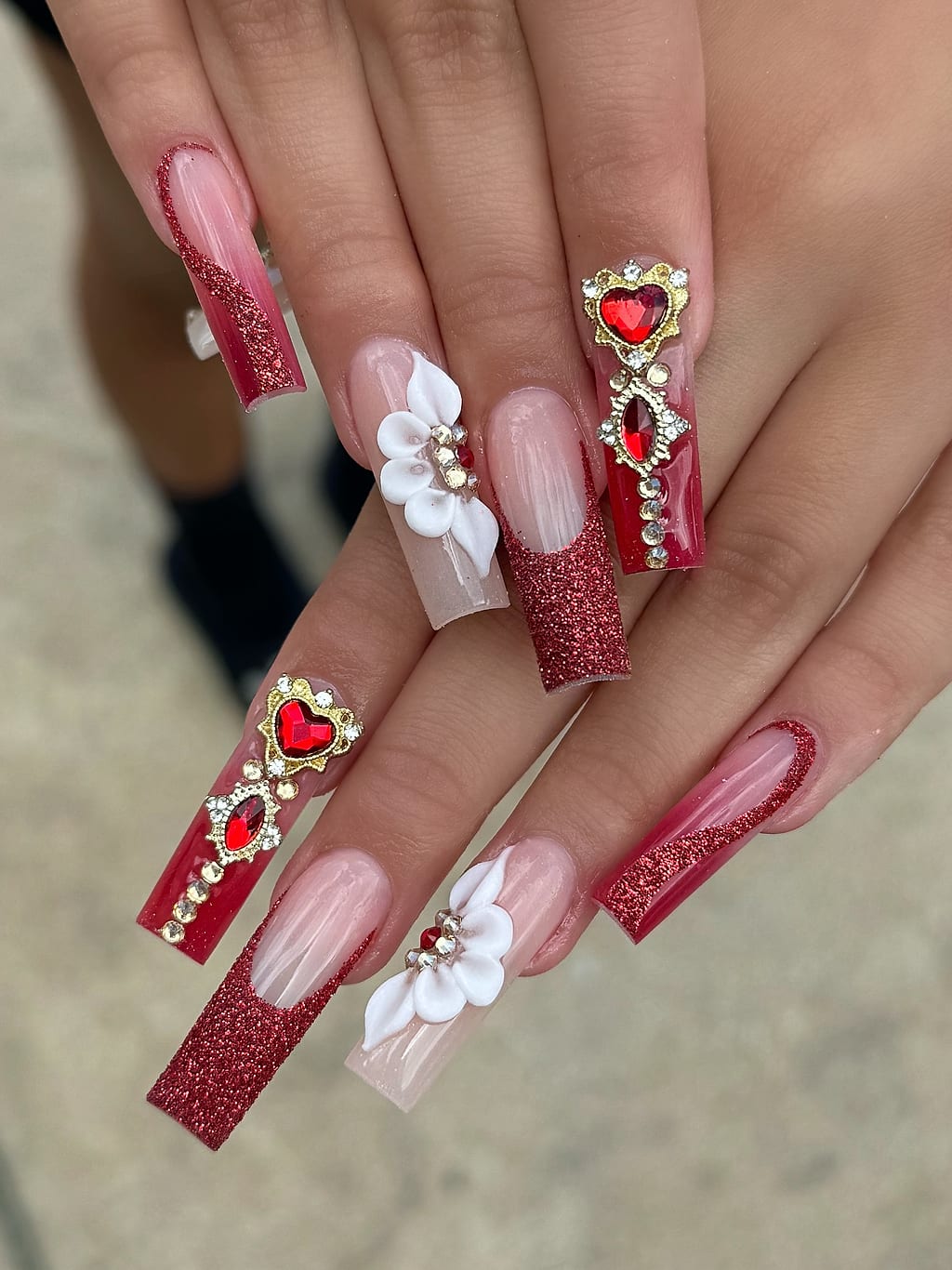Coffin nails with red glitter, white 3D flowers, and gem accents at Palace Nail Spa